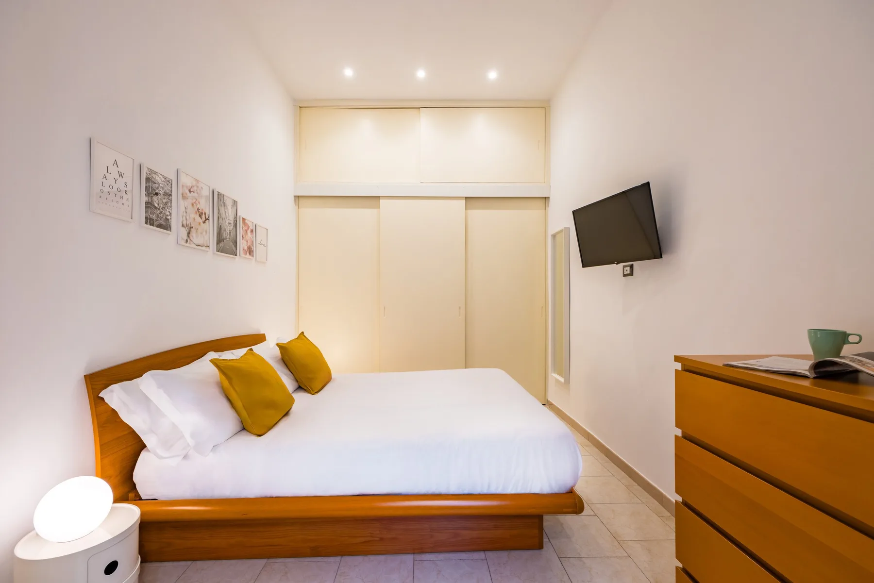 Un dormitorio con una cama, un televisor en la pared y una cómoda.