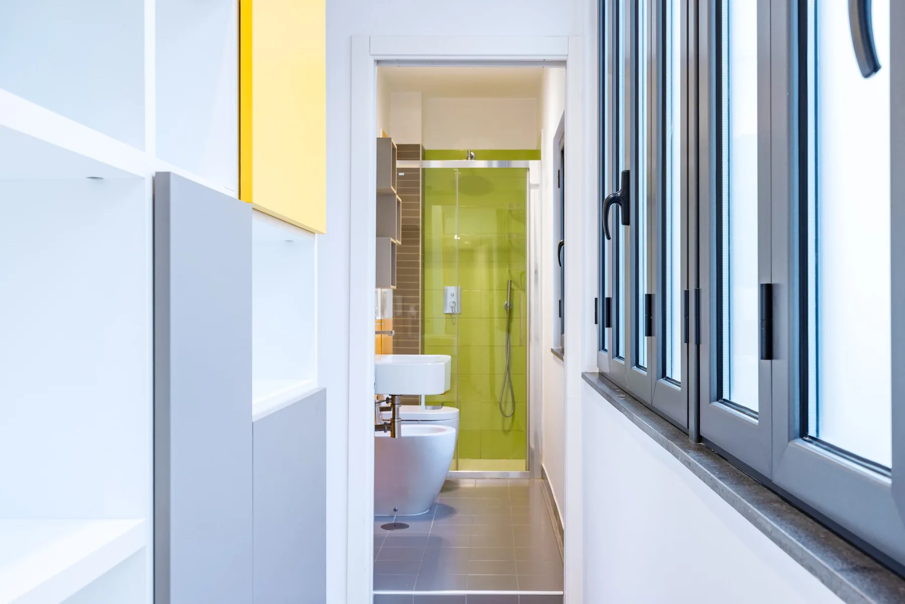 Baño estrecho con ducha, lavabo y una hilera de ventanas.