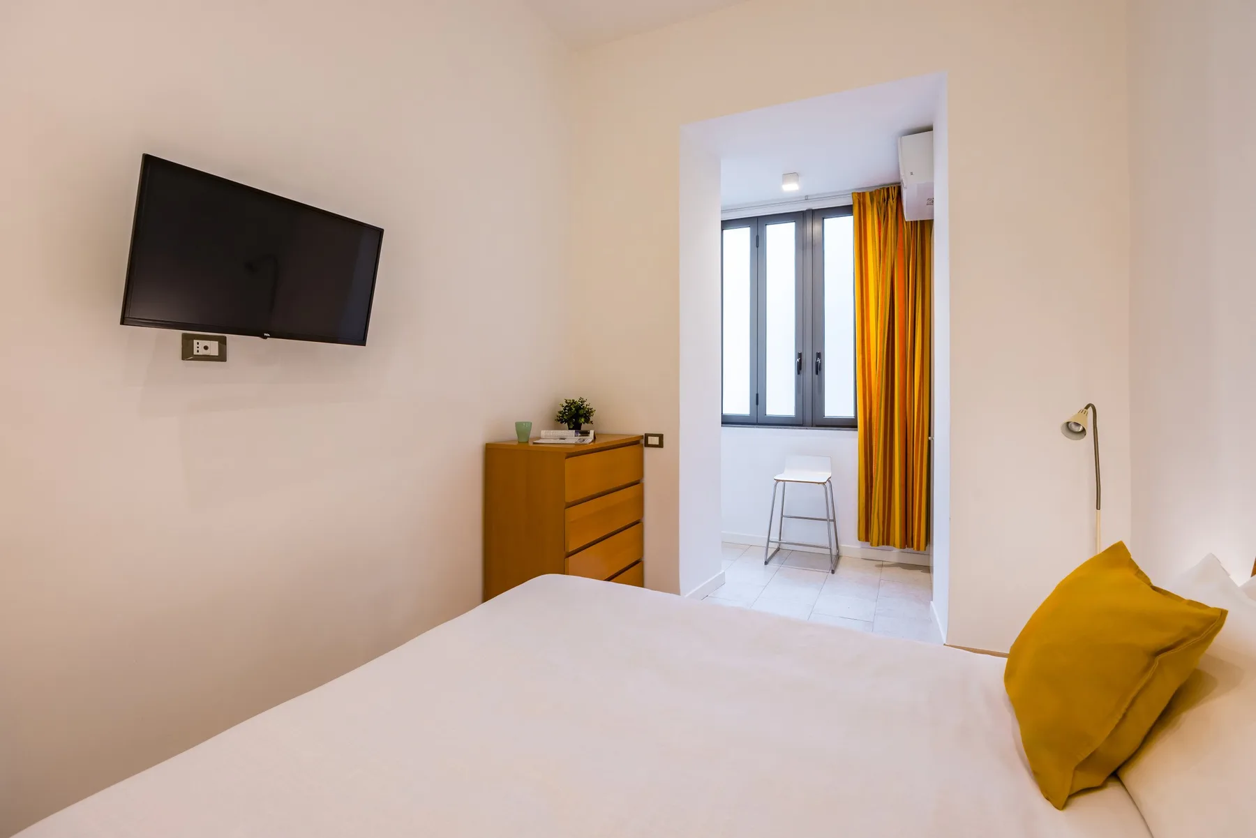 Un dormitorio con una cama, una cómoda y una ventana con cortinas amarillas.