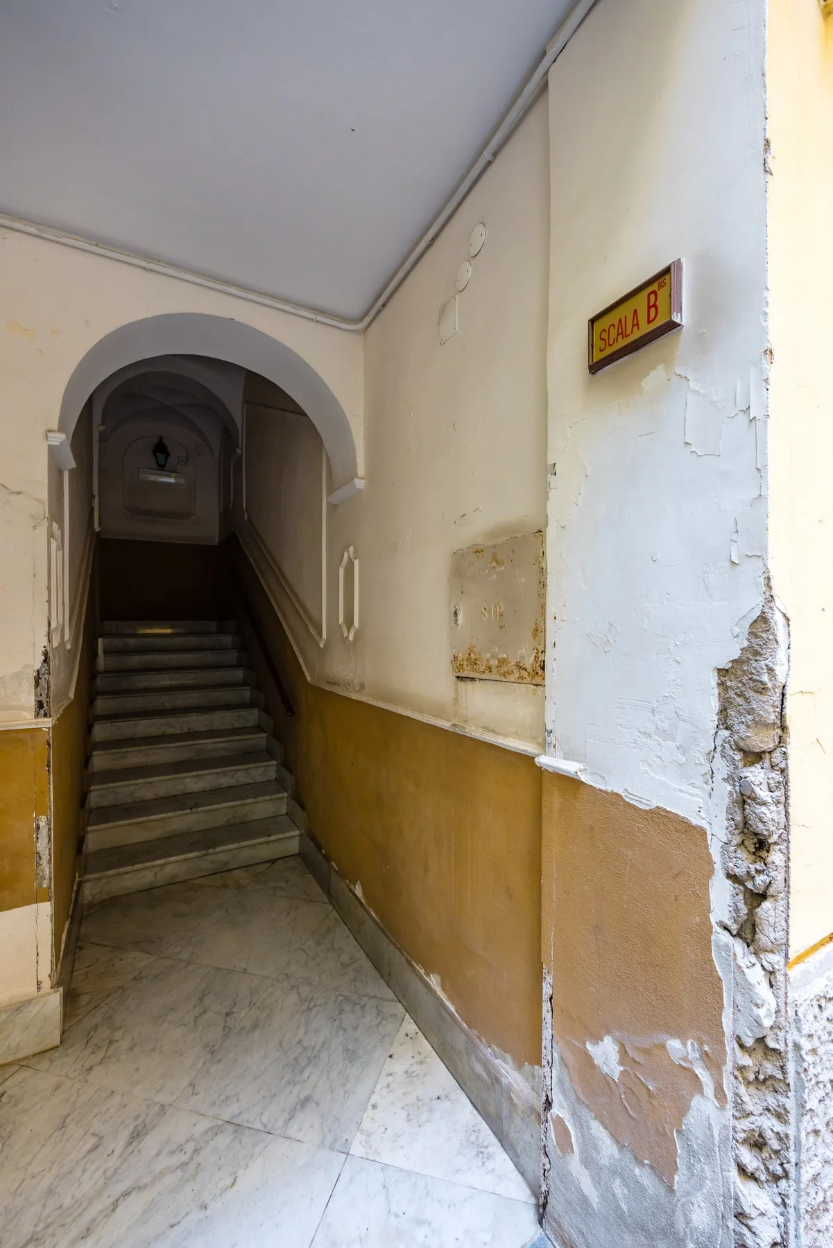 Una escalera interior desgastada con entrada arqueada y paredes pintadas.