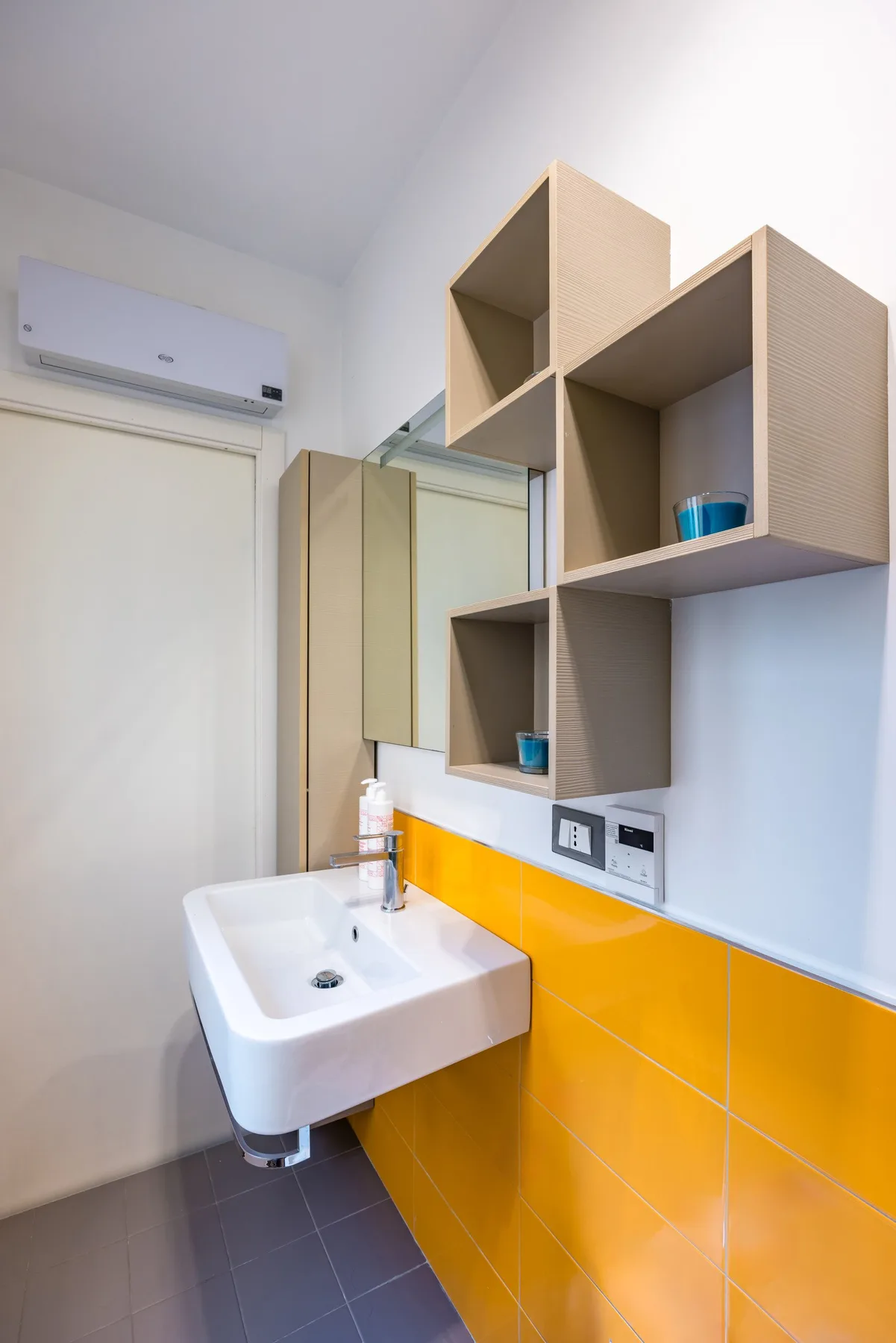 Un baño con lavabo suspendido, pared de azulejos naranjas y estantes abiertos.