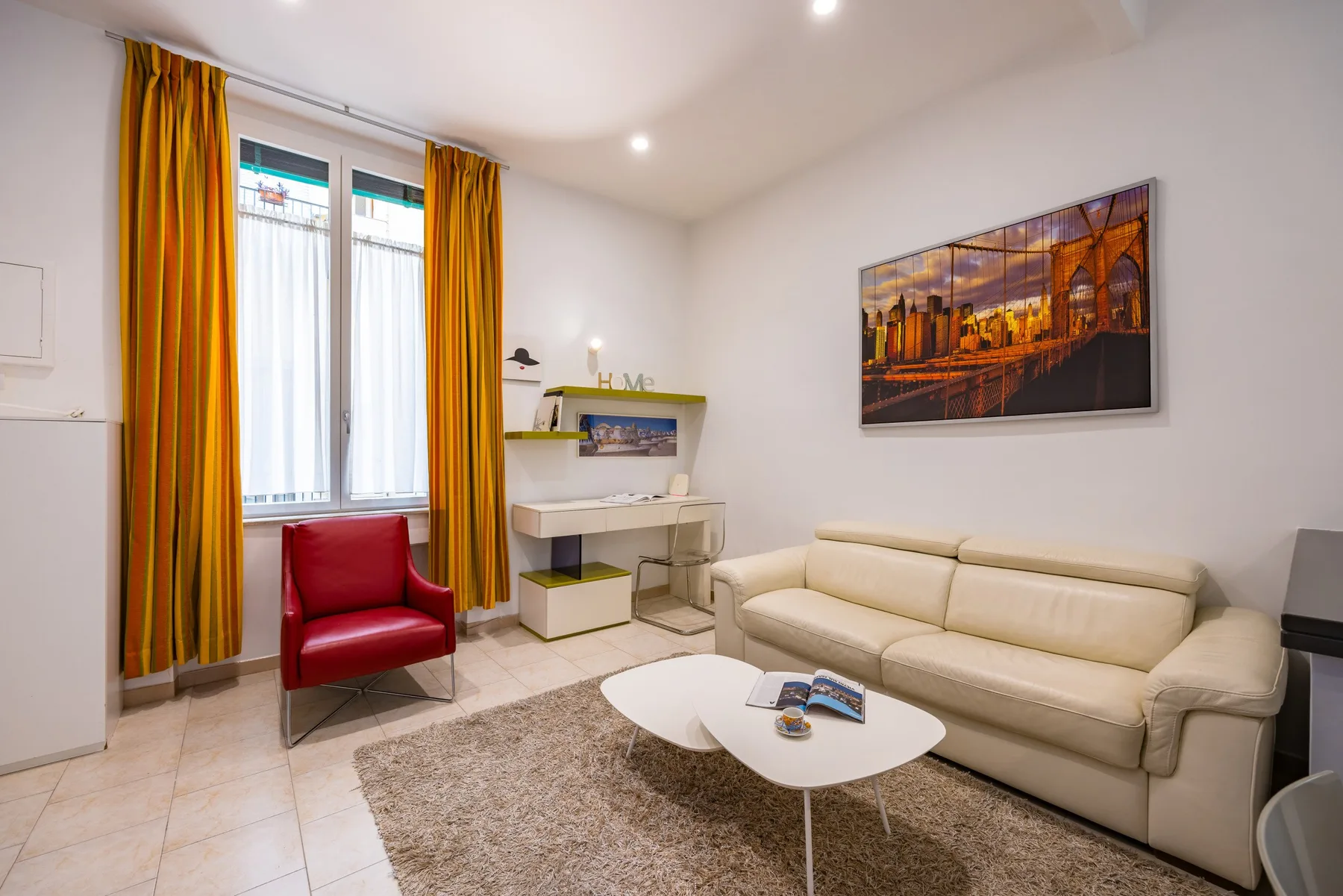 Una sala luminosa con un sofá color crema, un sillón rojo y una mesa de centro.