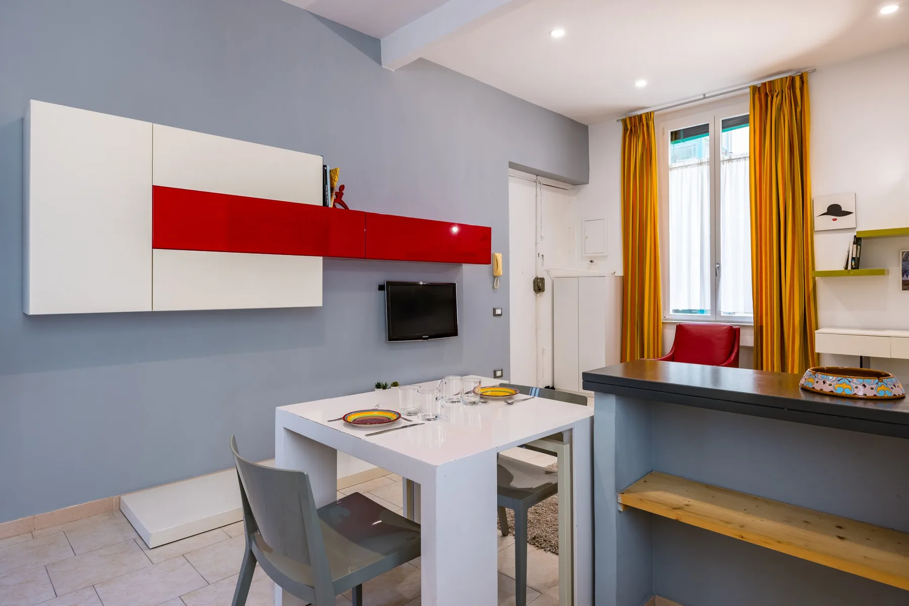 Un comedor compacto con una mesa blanca, sillas y un televisor montado en la pared.