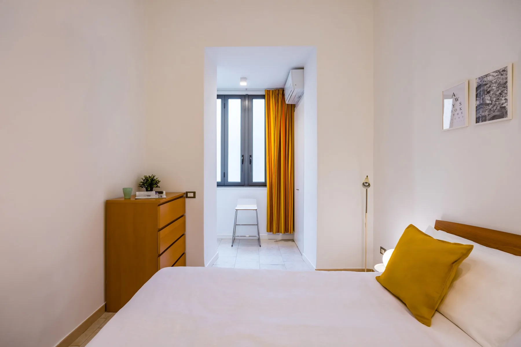 Un dormitorio con una cama, una cómoda de madera y una ventana con cortinas amarillas.