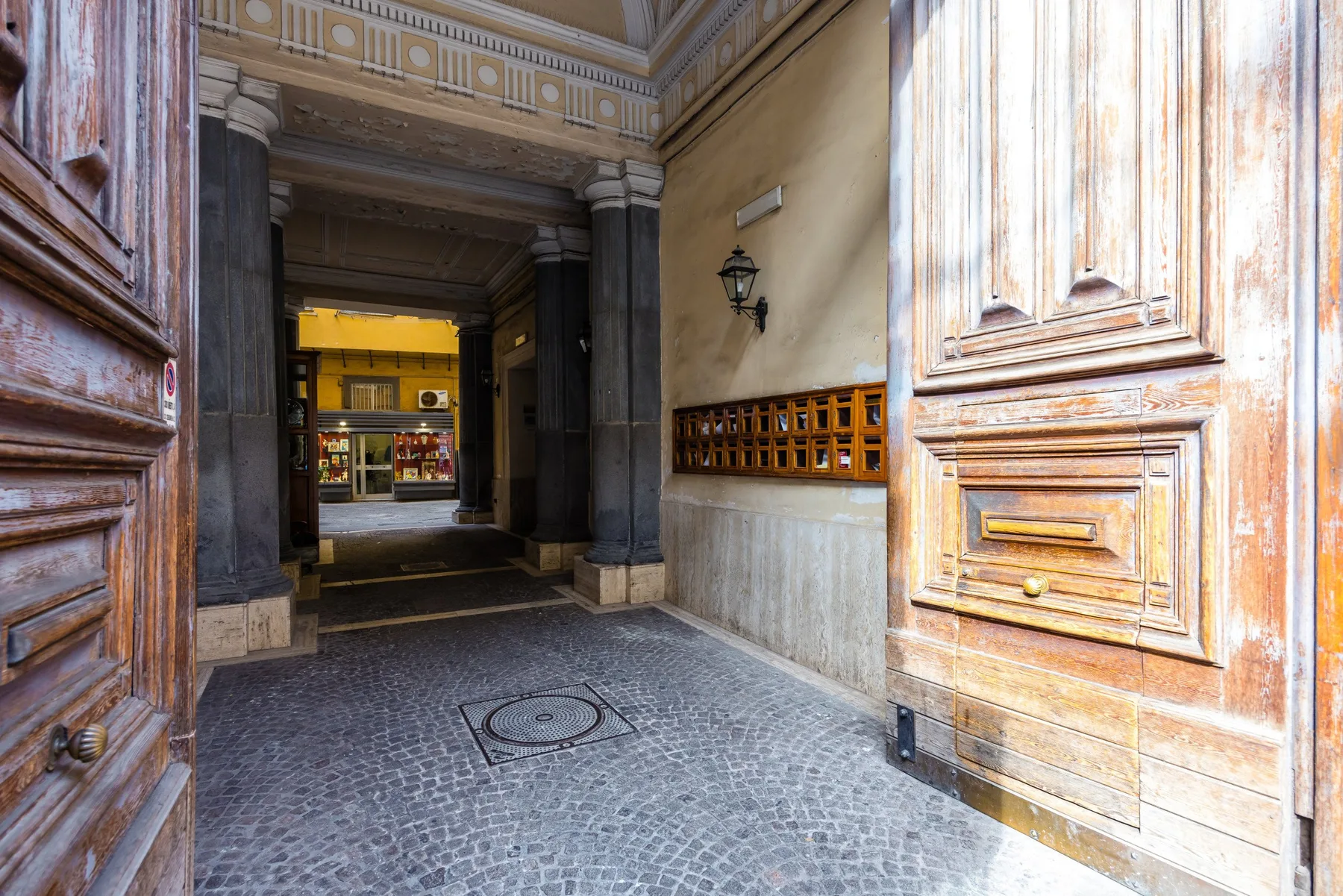 Un pasaje de entrada pavimentado en piedra, enmarcado por puertas de madera abiertas y columnas.