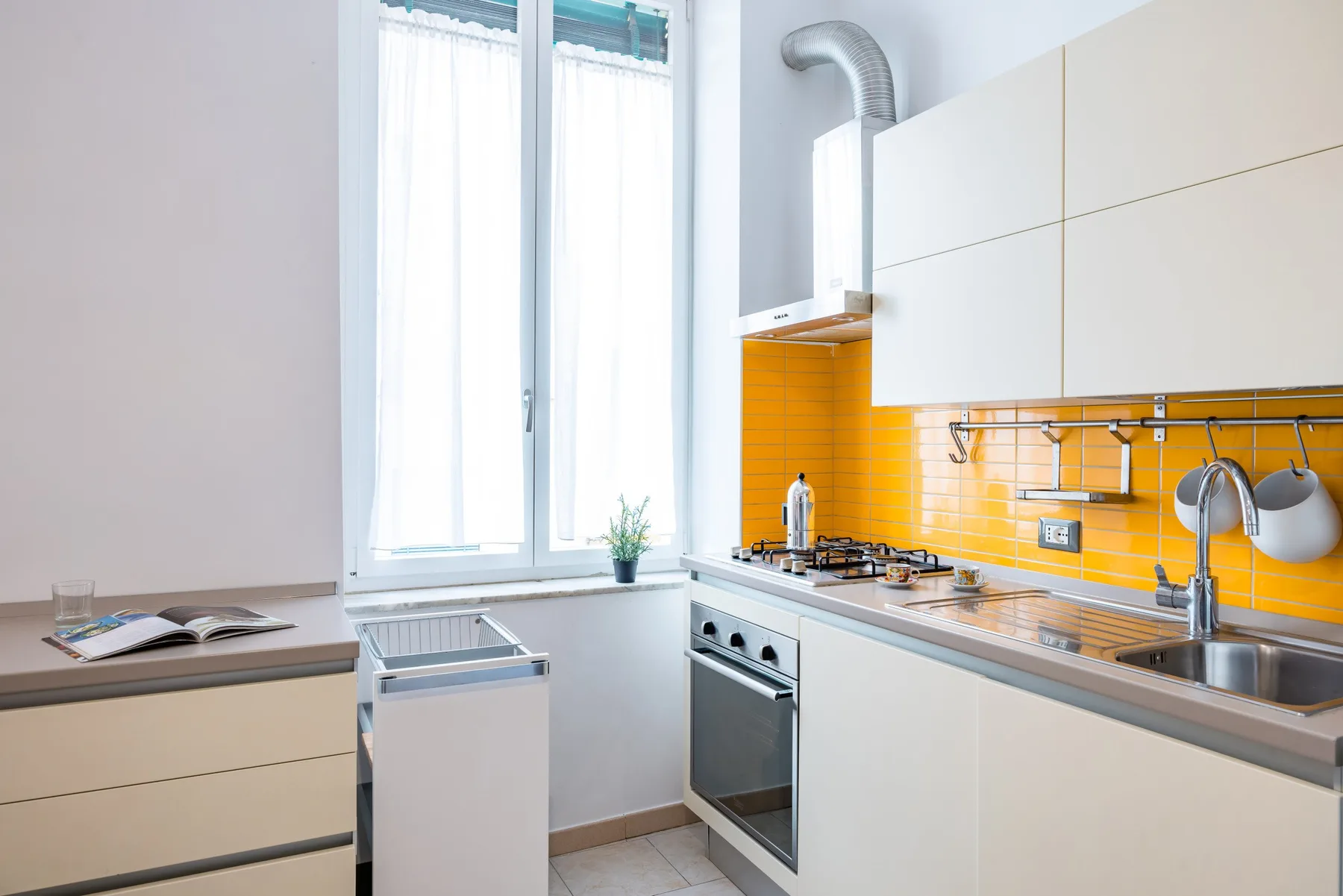Una cocina luminosa con armarios blancos, un salpicadero naranja y una ventana.