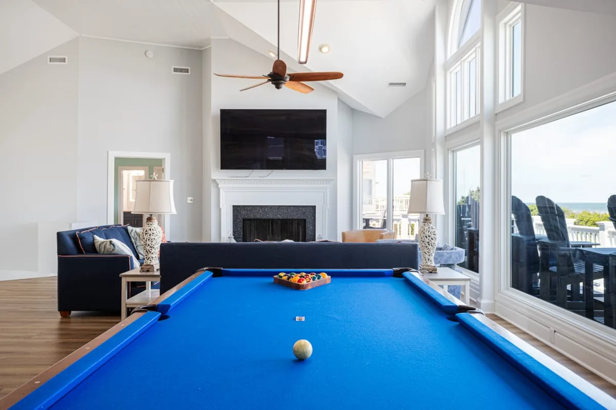 Una sala luminosa con una mesa de billar azul y ventanas grandes.