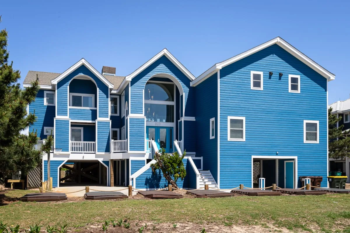 A large blue multi-story building stands beside a grassy yard under a clear sky.