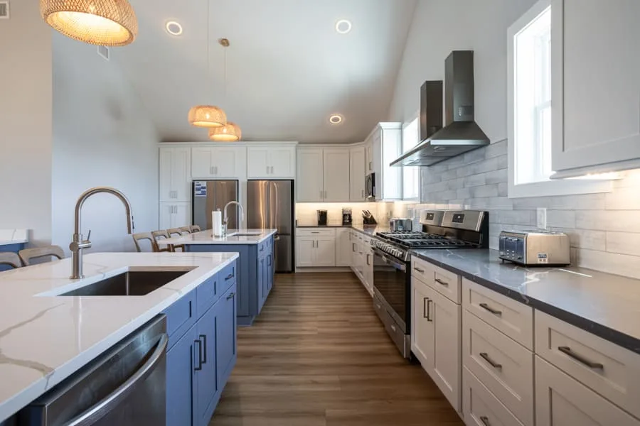 Una cocina luminosa con una isla azul, gabinetes blancos y electrodomésticos de acero inoxidable.