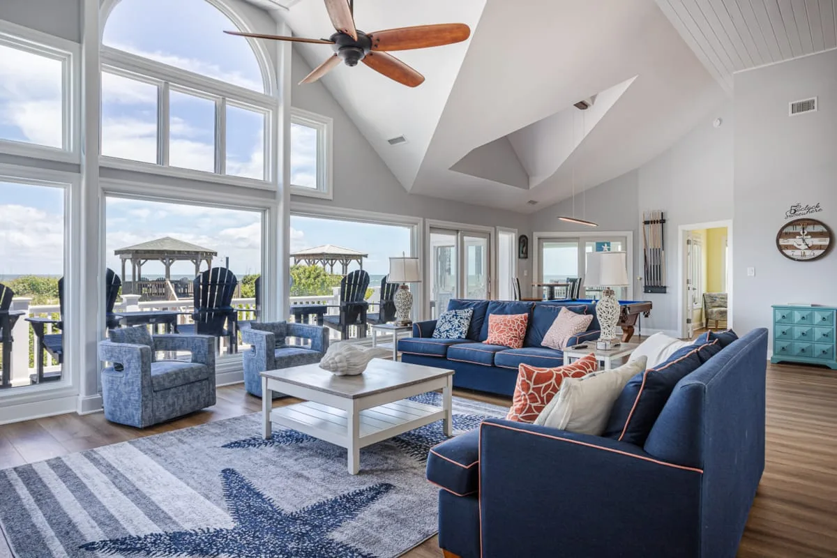 A bright living room opens onto a patio through large windows, with blue seating and a coffee table.