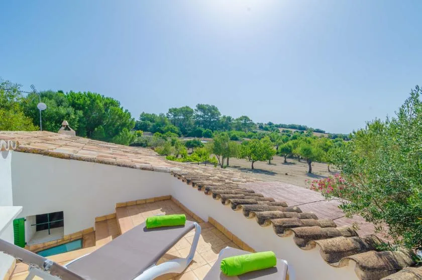 A sunny outdoor terrace overlooks a green landscape, with lounge seating in the foreground.