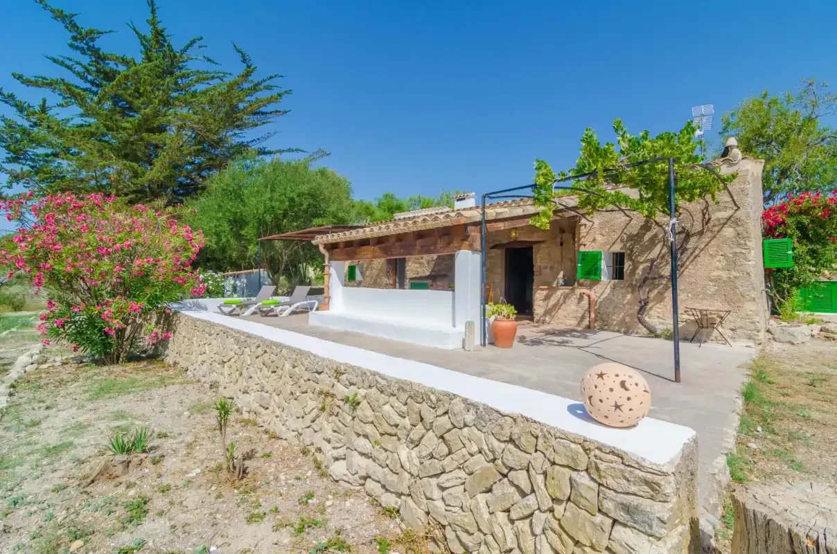 A stone house with a raised patio, outdoor seating, and flowering shrubs.