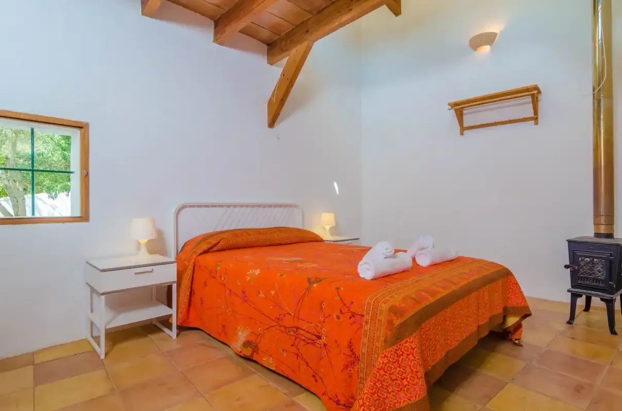 A bedroom with an orange bedspread and exposed wooden ceiling beams.