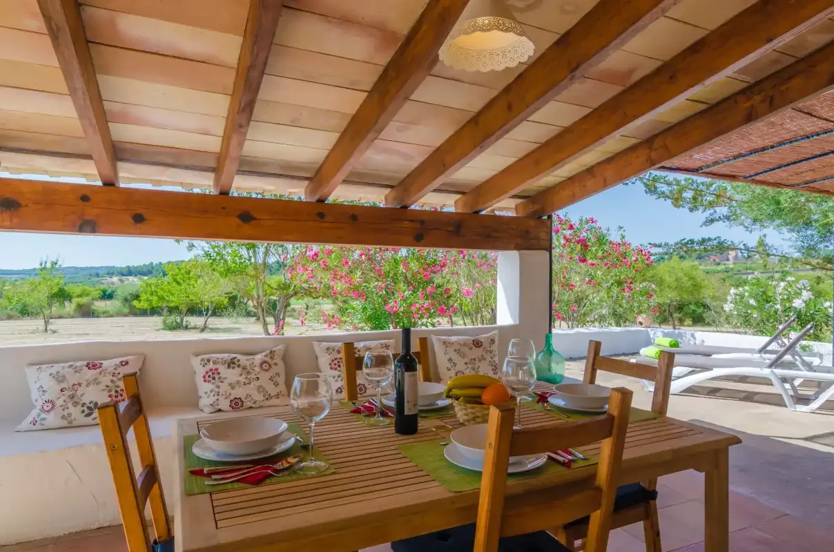 A covered outdoor dining area with a wooden table overlooks a garden.