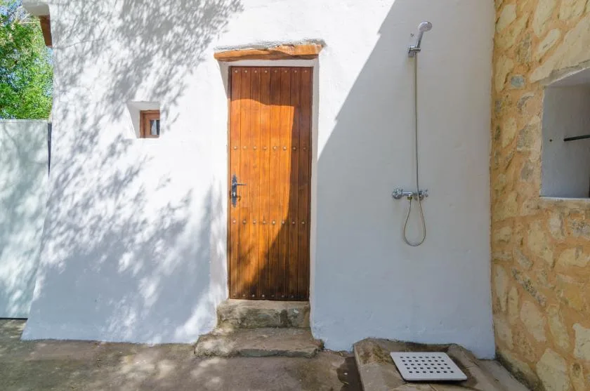 An outdoor shower beside a wooden door on a white stucco wall.