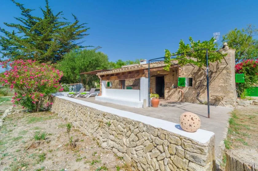 Outdoor patio beside a stone building, with lounge seating and flowering shrubs.