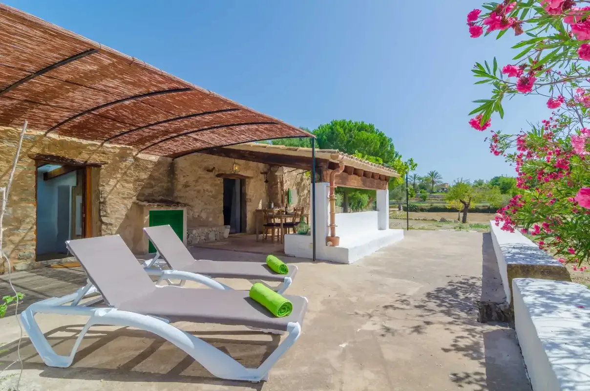 A stone outdoor patio with lounge seating beneath a shaded pergola.