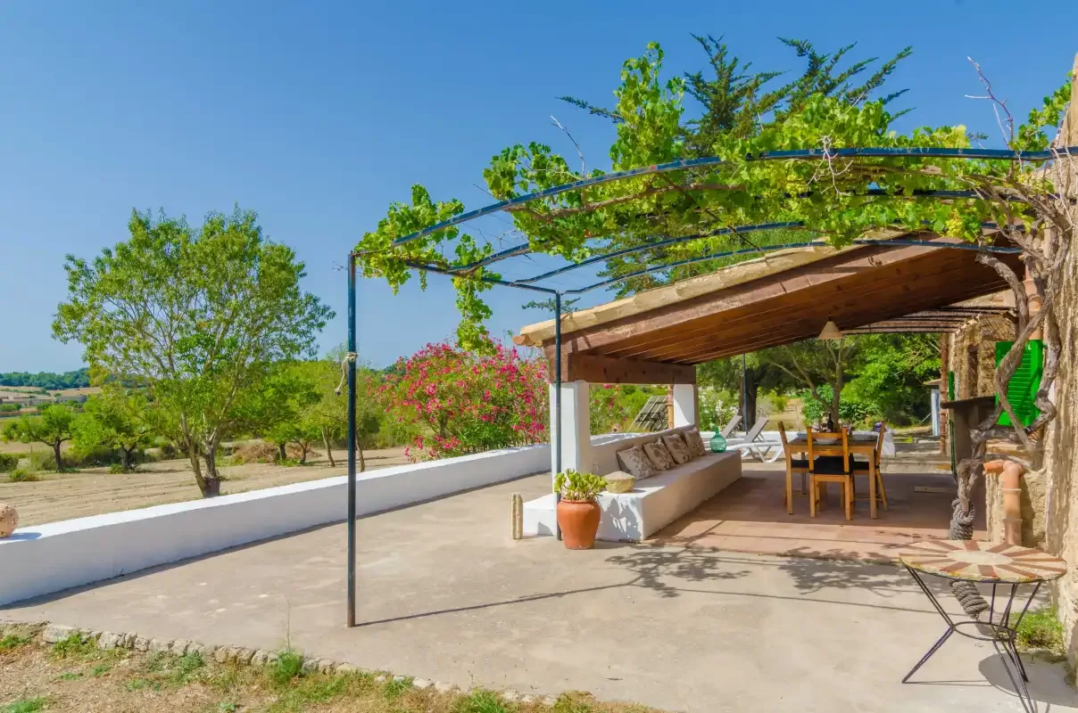 An outdoor patio with a wooden pergola, dining table, and surrounding greenery.