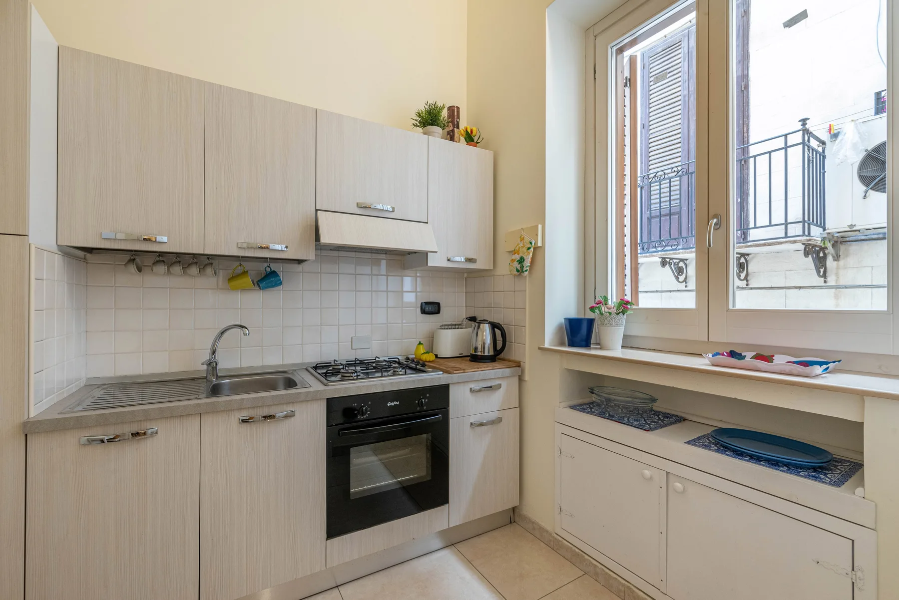 A bright kitchen with light cabinets, a stovetop, and a large window.