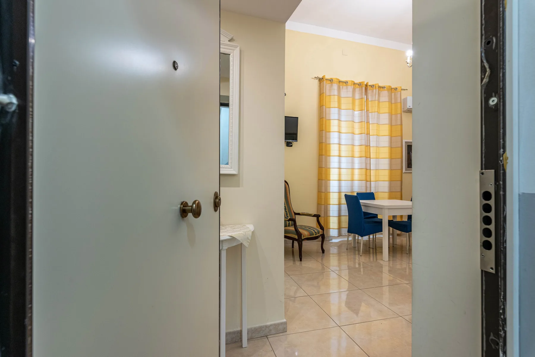 A doorway opens onto a dining area with a table, chairs, and checked curtains.
