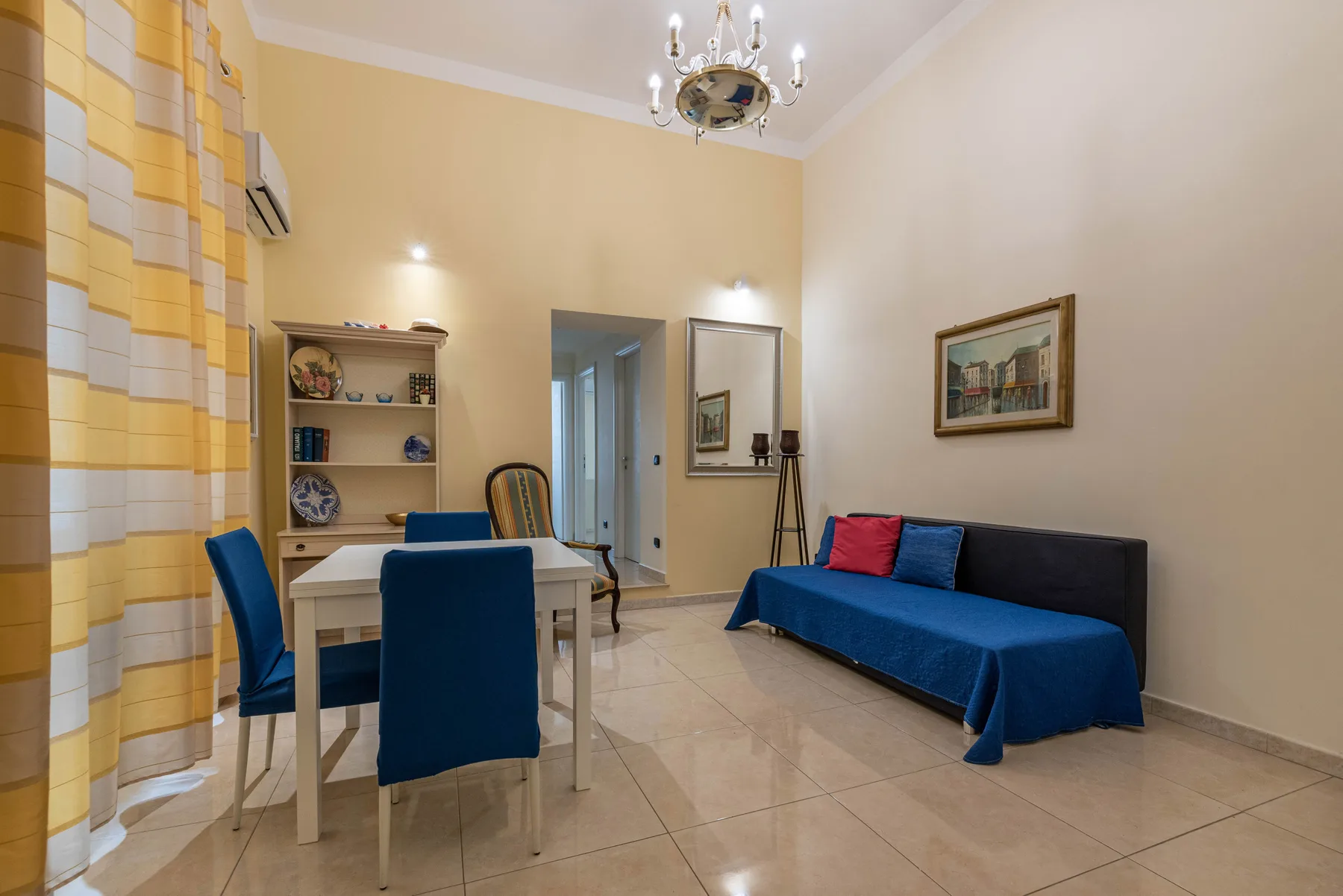 Una sala de estar con un sofá azul y una mesa de comedor junto a cortinas estampadas.