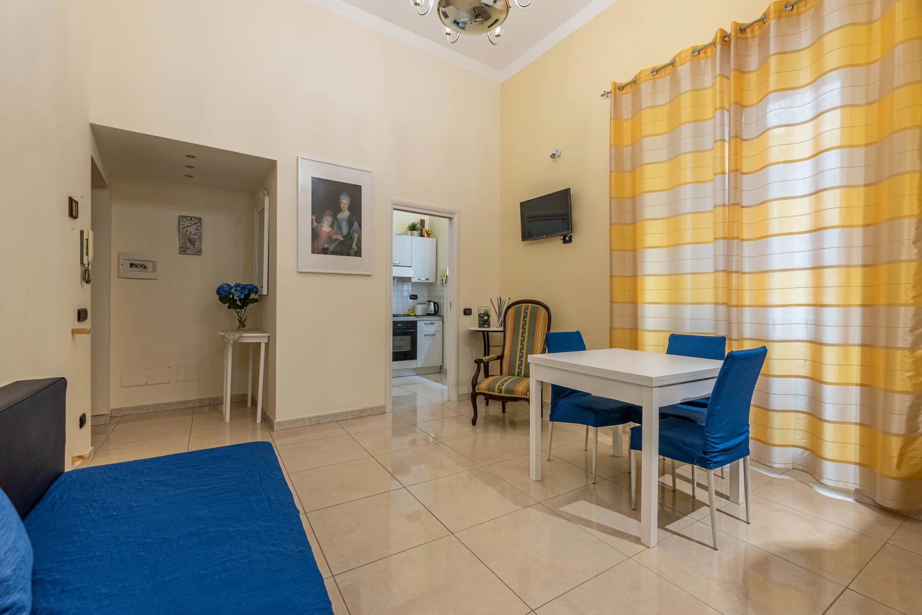 Zona de comedor y estar con una mesa blanca, asientos azules y cortinas a rayas.