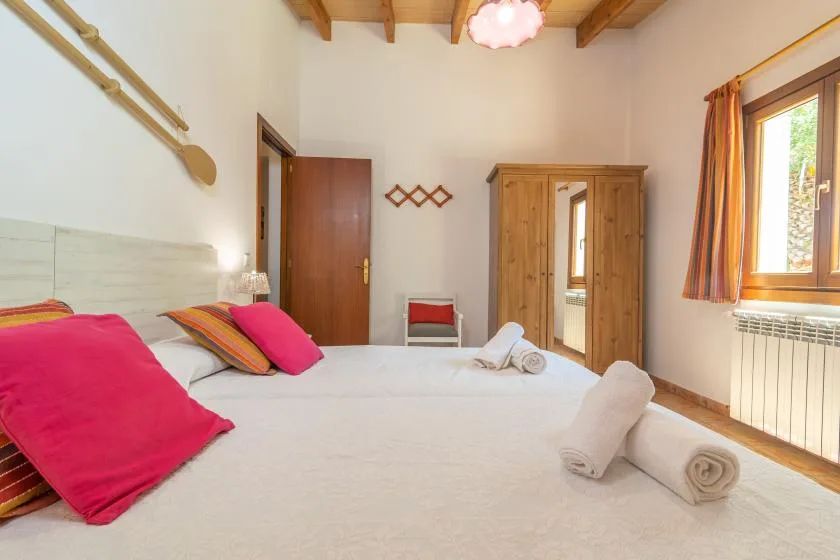 A bedroom with a bed, colorful pillows, and a wooden wardrobe.