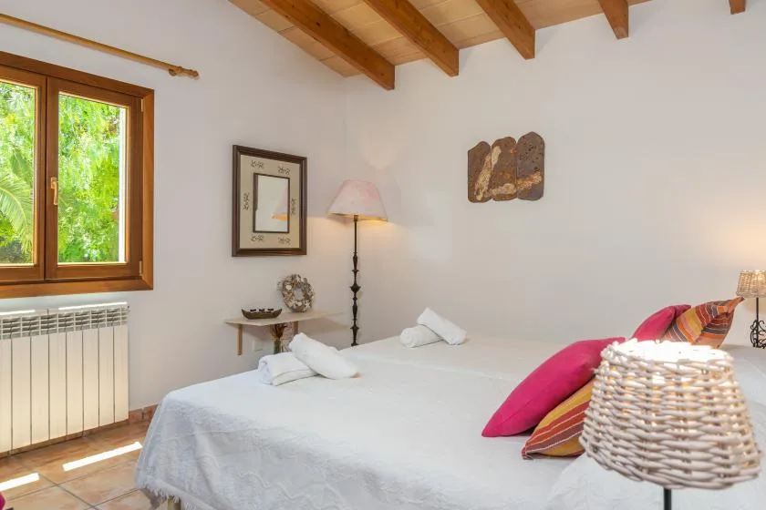 A bedroom with a large bed, colorful pillows, and exposed wooden ceiling beams.