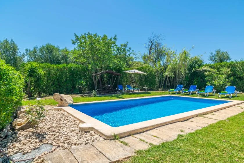 An outdoor swimming pool sits beside a stone path and green lawn.