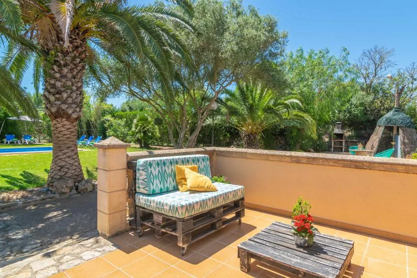 A tiled outdoor patio has a cushioned bench, low table, and potted flowers.