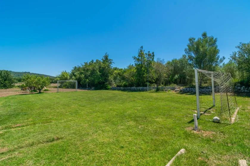 A grassy outdoor sports field with soccer goals and trees along the edge.