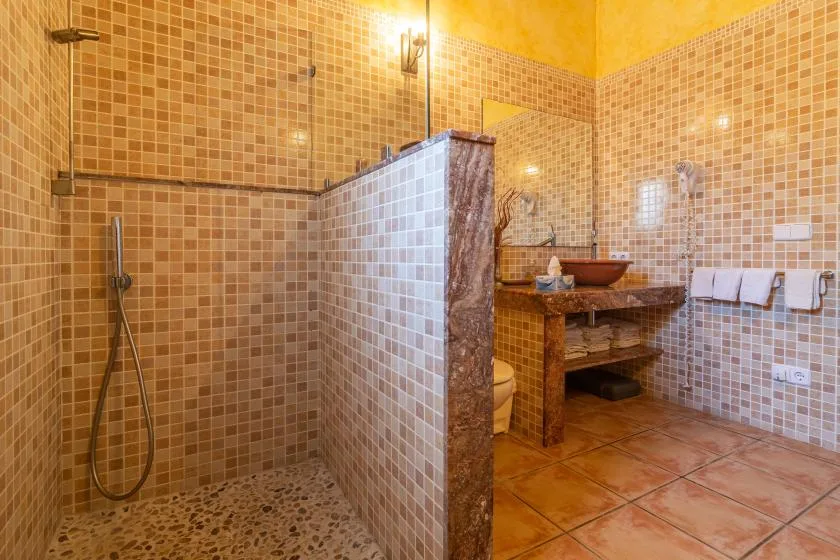 A tiled bathroom with a shower area, sink, and towels.