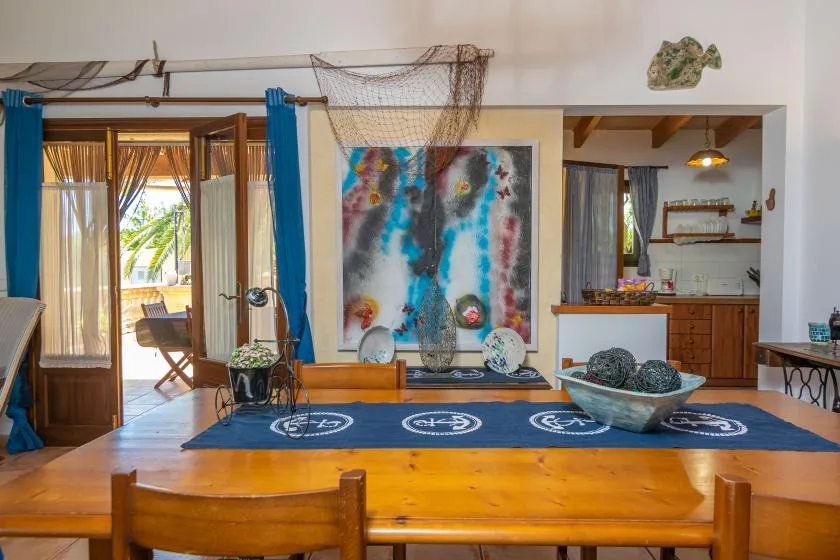 A dining area with a wooden table, colorful wall art, and an open kitchen.