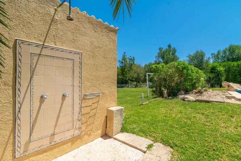 An outdoor shower area beside a grassy garden under a clear blue sky.