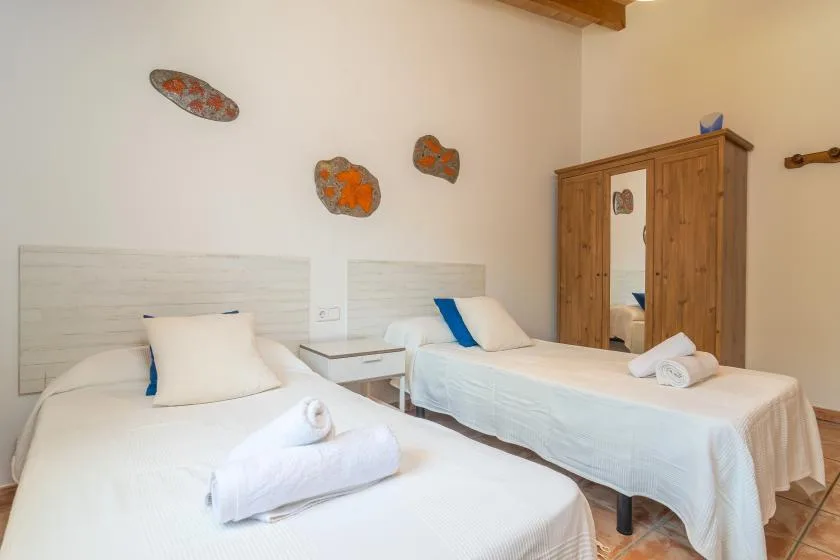 A bedroom with two beds, white bedding, and a wooden wardrobe.