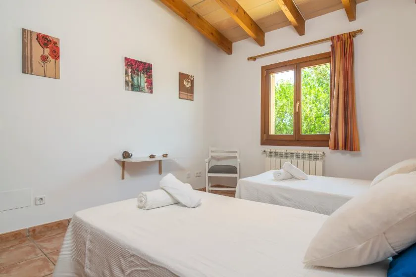 A bedroom with two beds, a window, and exposed wooden ceiling beams.