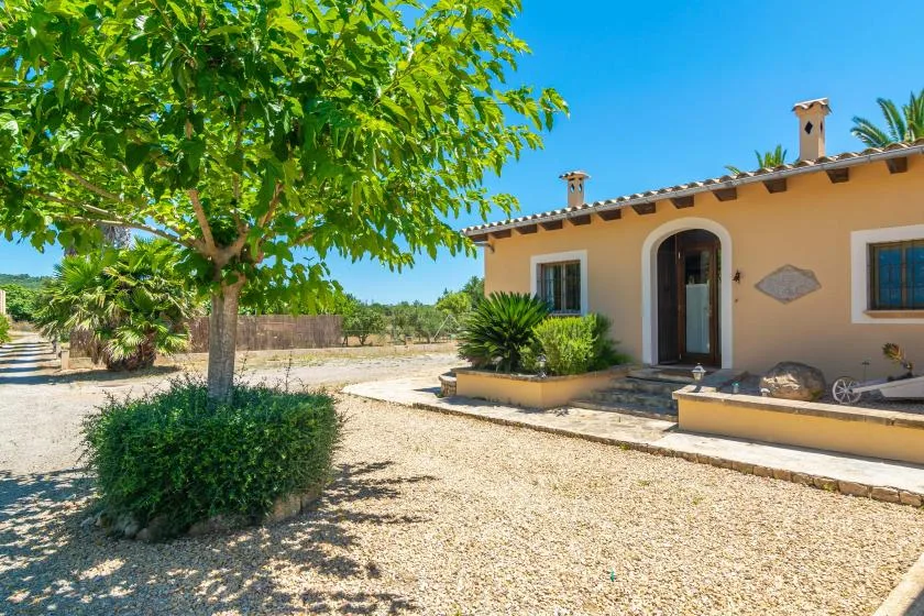 A house exterior with a gravel courtyard and leafy trees.