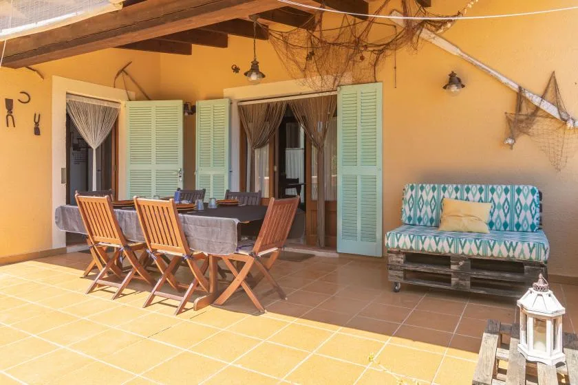 A covered patio features a dining table with folding chairs and a cushioned bench.