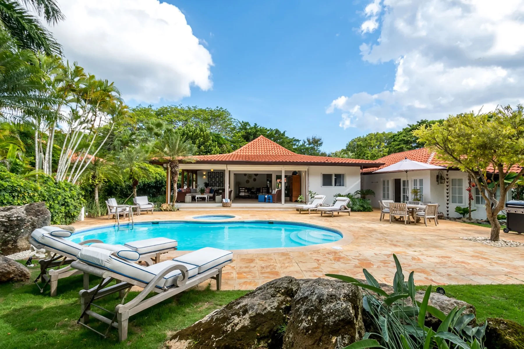 Una piscina exterior está junto a un patio de baldosas y una casa baja.