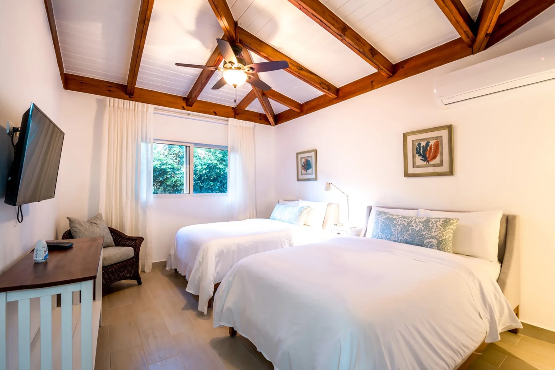 Dormitorio luminoso con dos camas bajo vigas de madera expuestas.