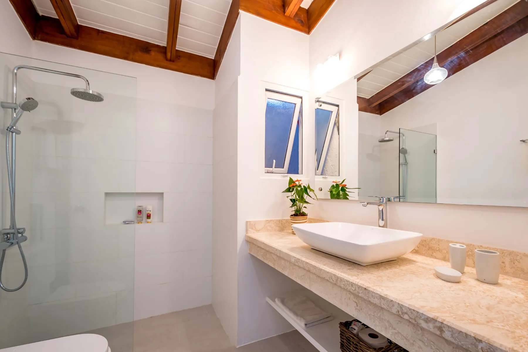 Un baño luminoso con una ducha de vidrio y una amplia encimera con lavabo.