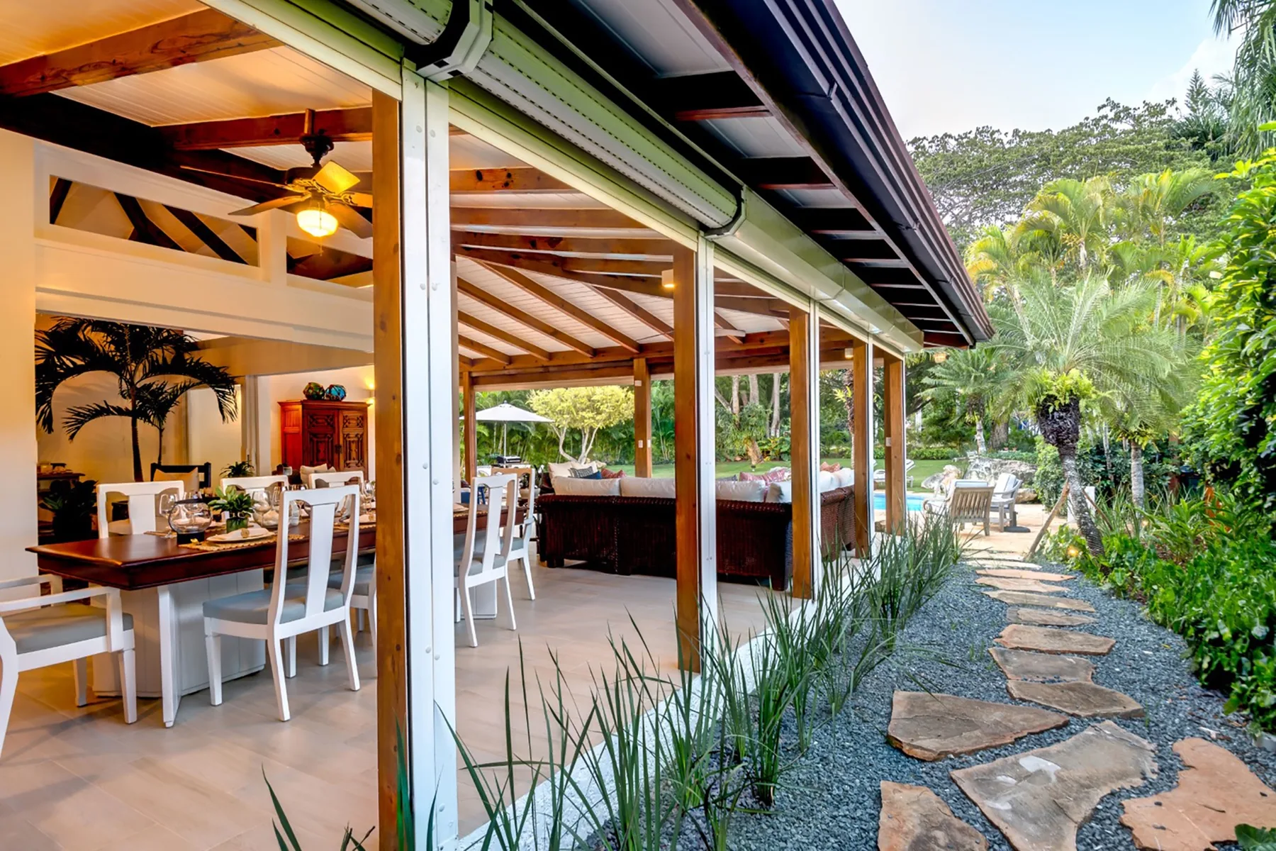 Un comedor cubierto se abre a un sendero de jardín rodeado de vegetación tropical.