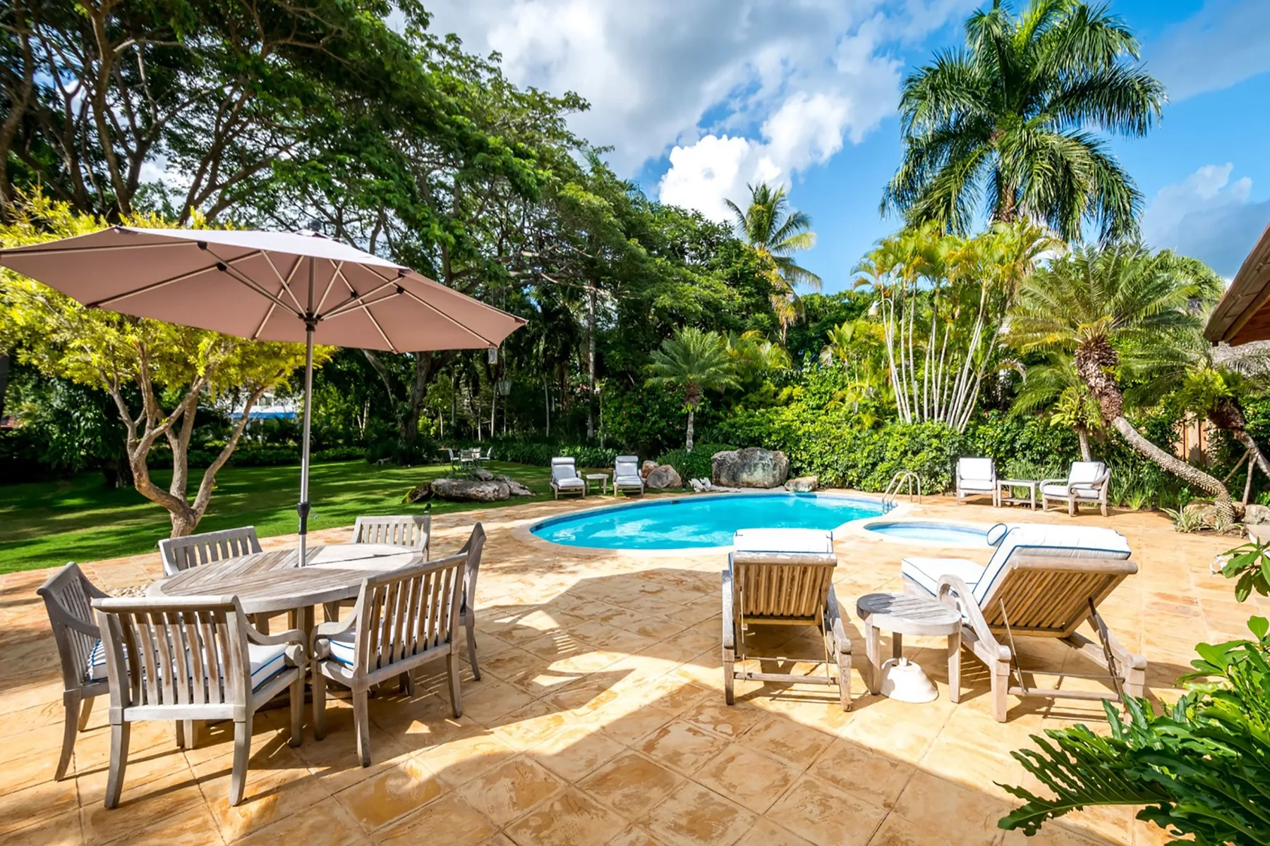 Una piscina está junto a una zona de estar al aire libre, rodeada de vegetación tropical.