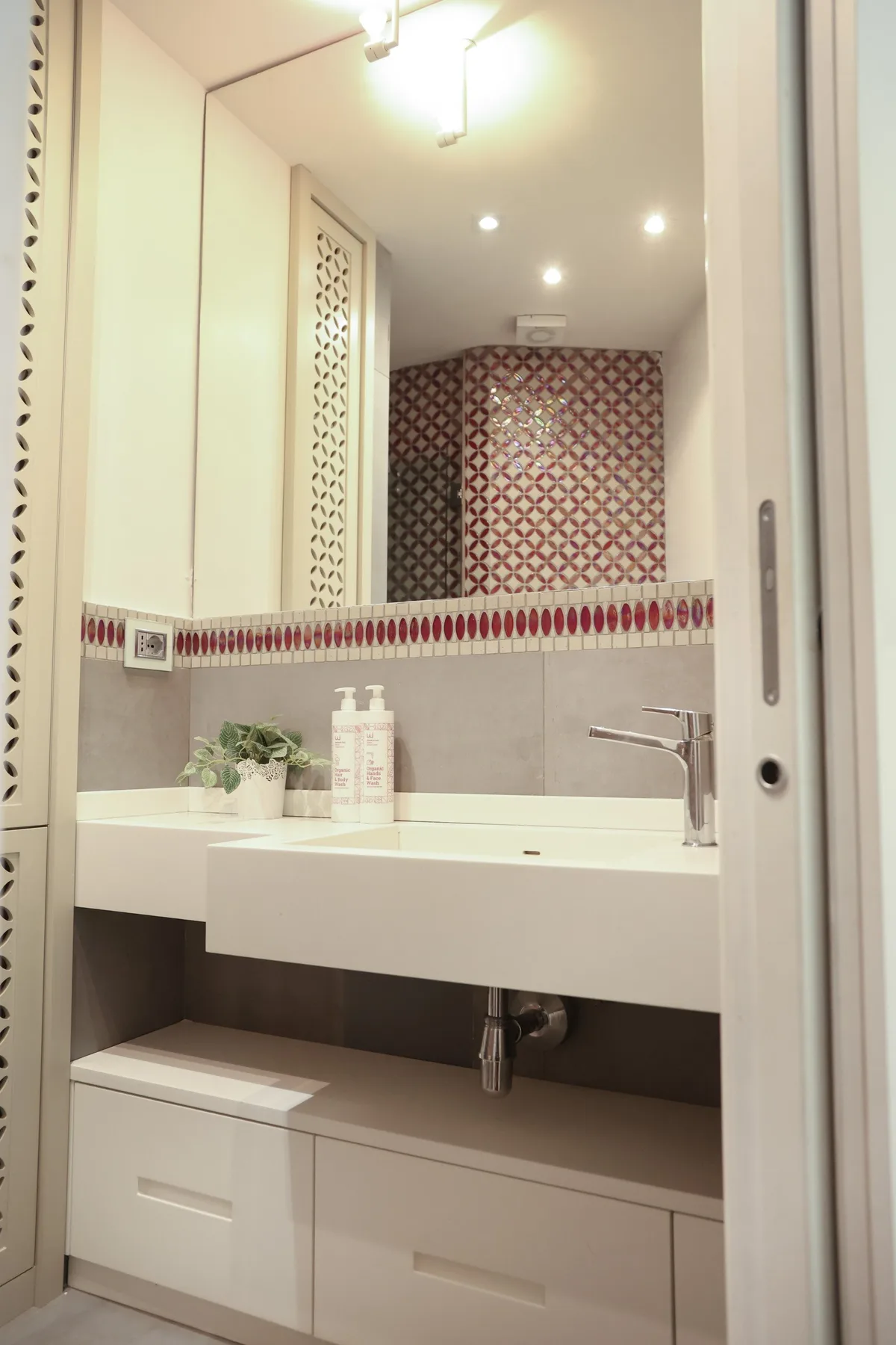 A bathroom vanity with a wide white sink, wall mirror, and patterned tile border.