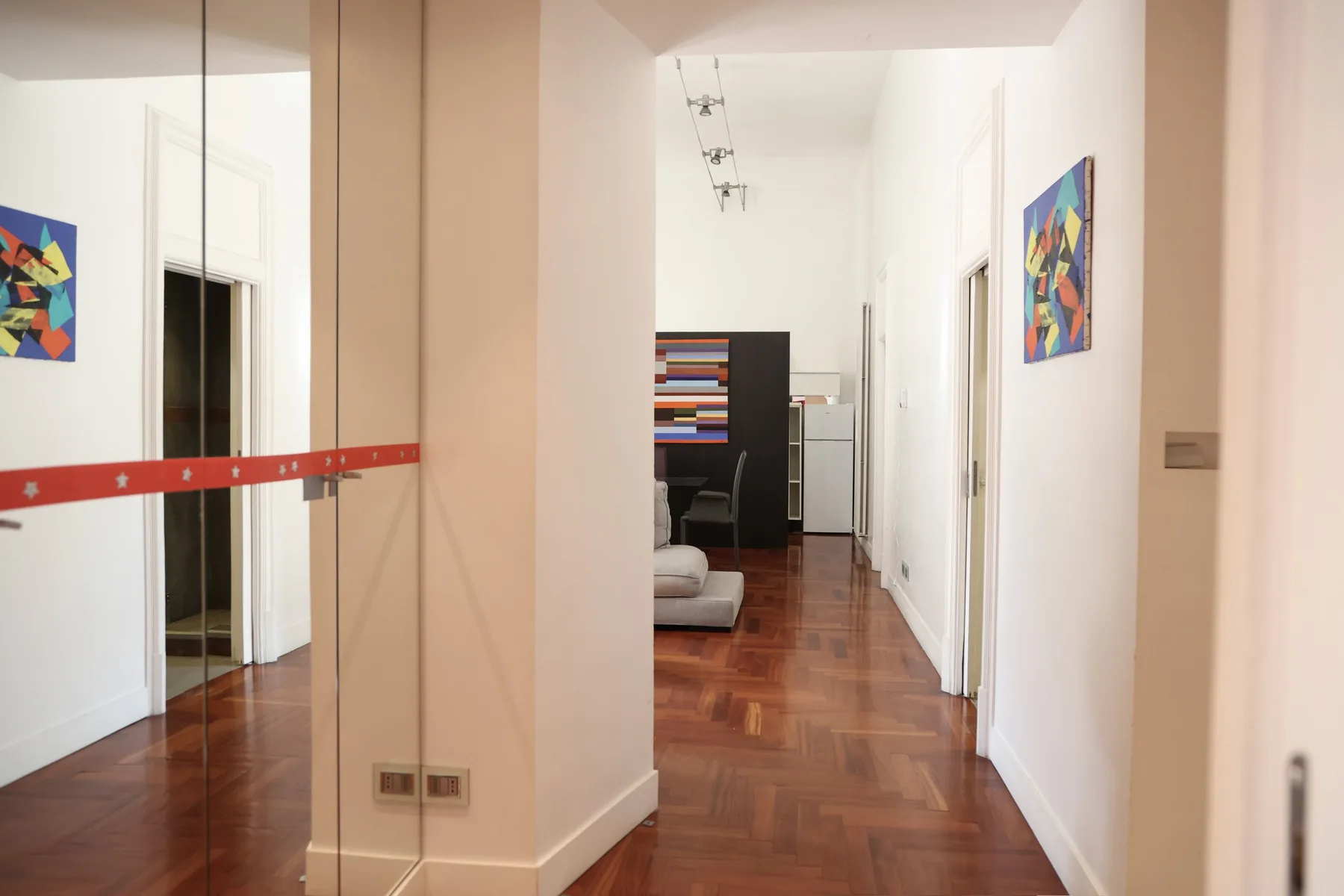 A hallway with polished wood flooring and colorful abstract paintings.
