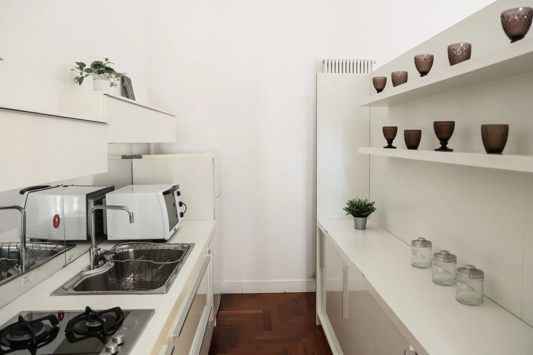 A bright kitchen with a sink, stovetop, and open shelves displaying pottery.