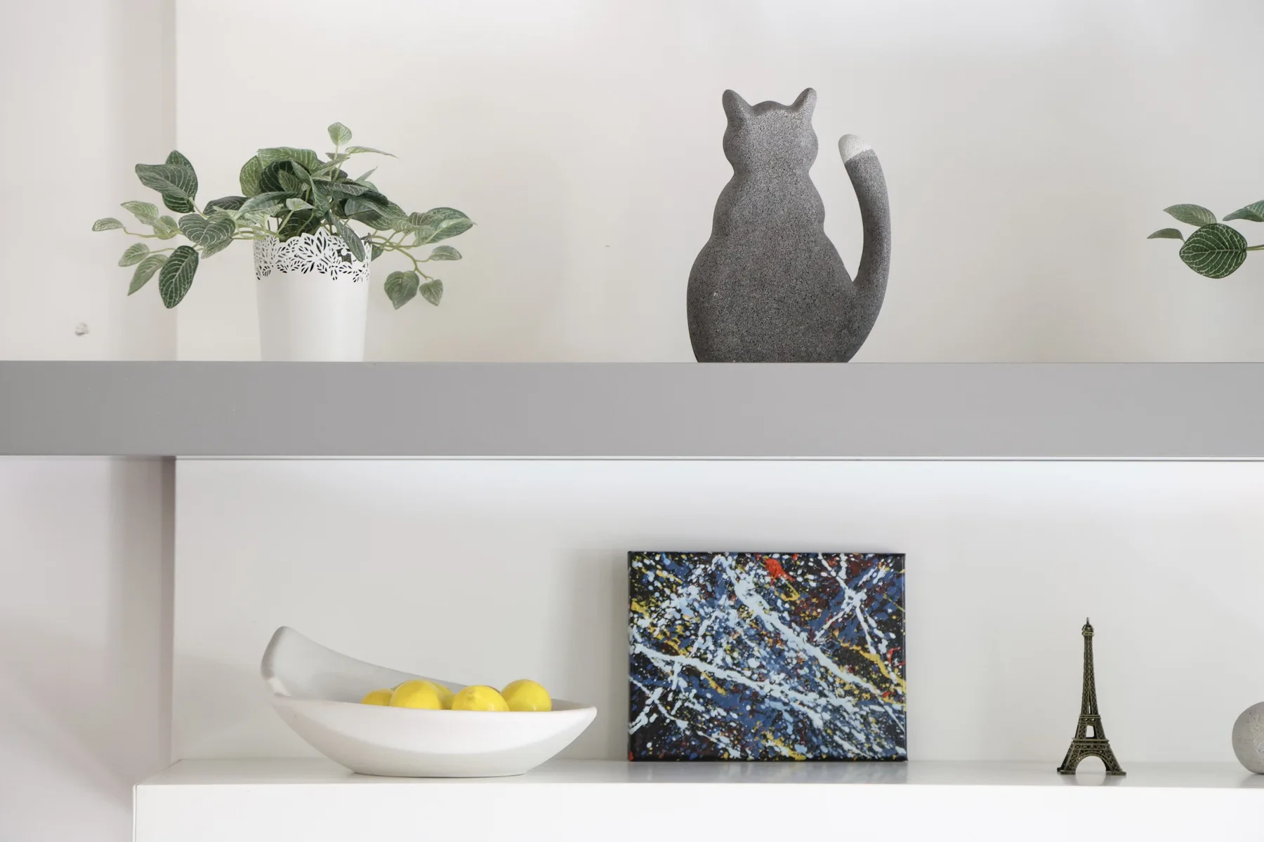 Decorative shelving displays plants, artwork, a cat-shaped sculpture, and small ornaments.