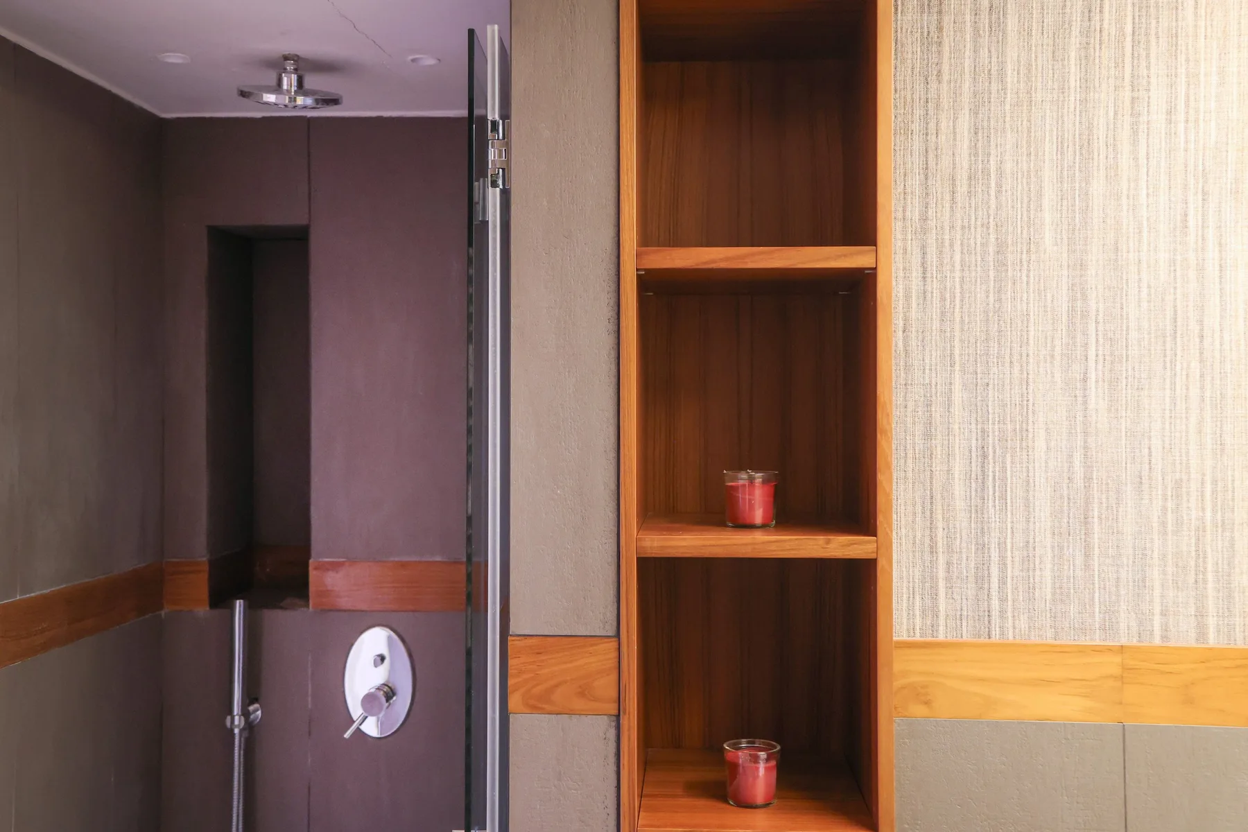 A bathroom shower area beside a wooden shelving unit.