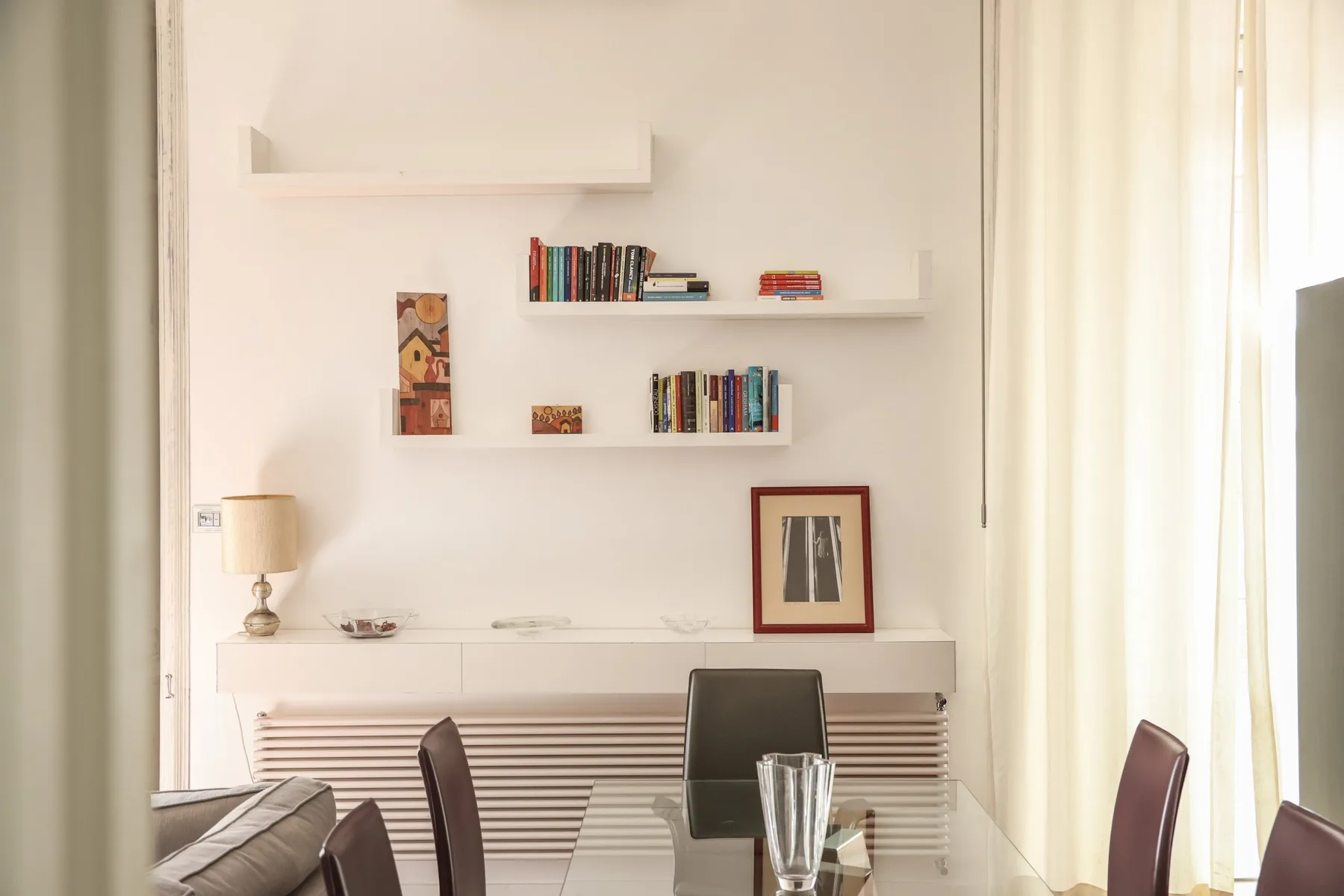 A bright living room with shelving and a dining table beside a window.