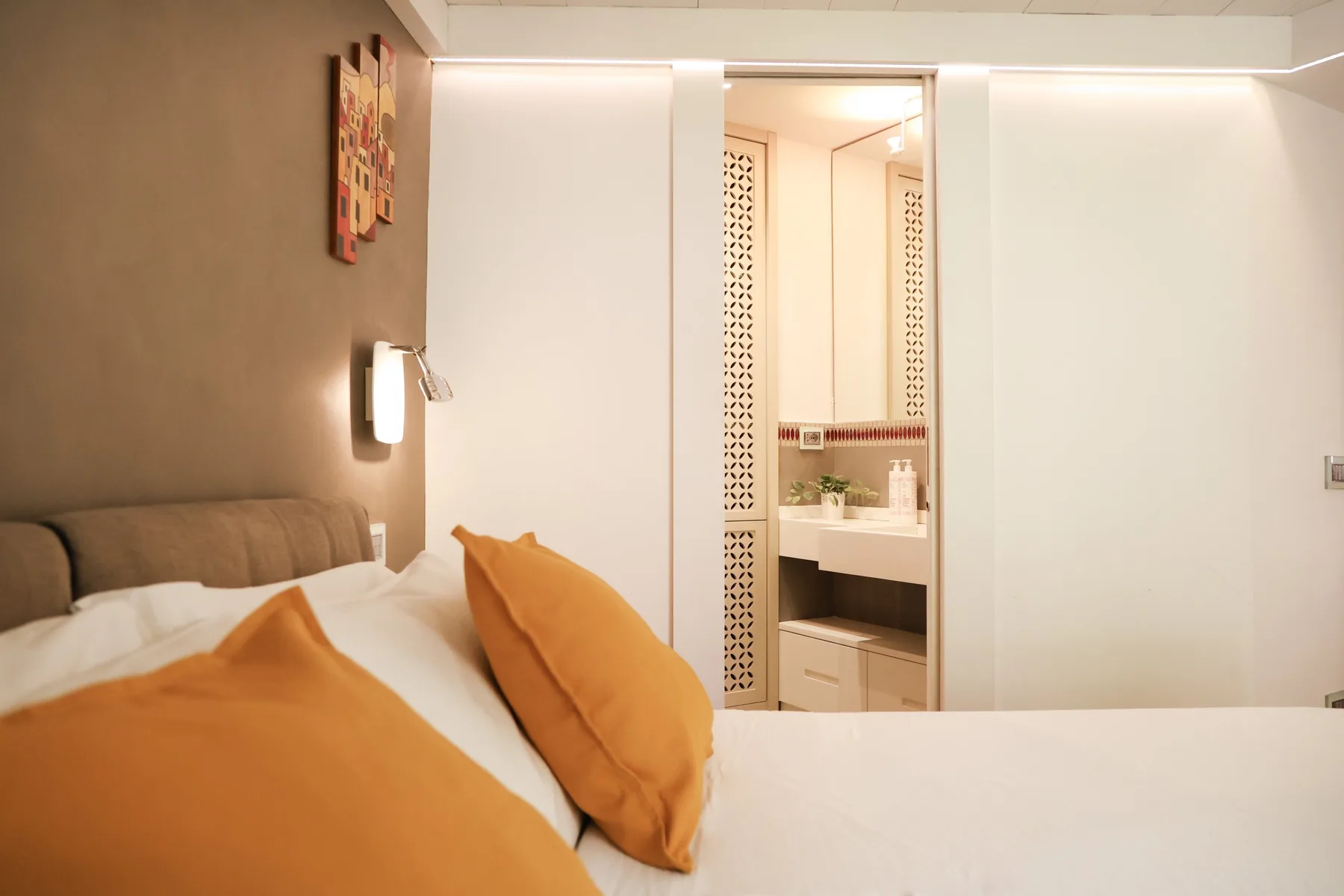 A bedroom with orange pillows beside an open vanity area.